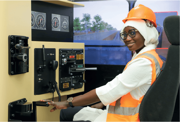 Une jeune femme en tenue de sécurité aux commandes d'un simulateur de conduite de train.